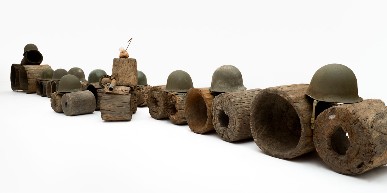 Gérard Quenum, Mort au dictateur. Vive la dictature! (Death to the Dictator. Long Live Dictatorship!), 2012. Wood, helmets, metal pipe, antenna and plastic doll, 75 x 637 x 105 cm.